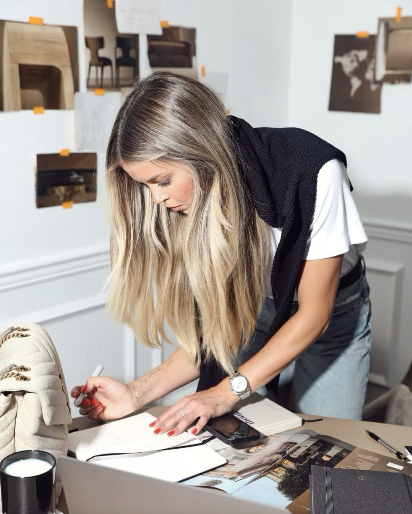 Blonde woman creating mood board leaning over desk with pinned inspiration photos notes and laptop in chic creative workspace showcasing Build Visibility Through PR.