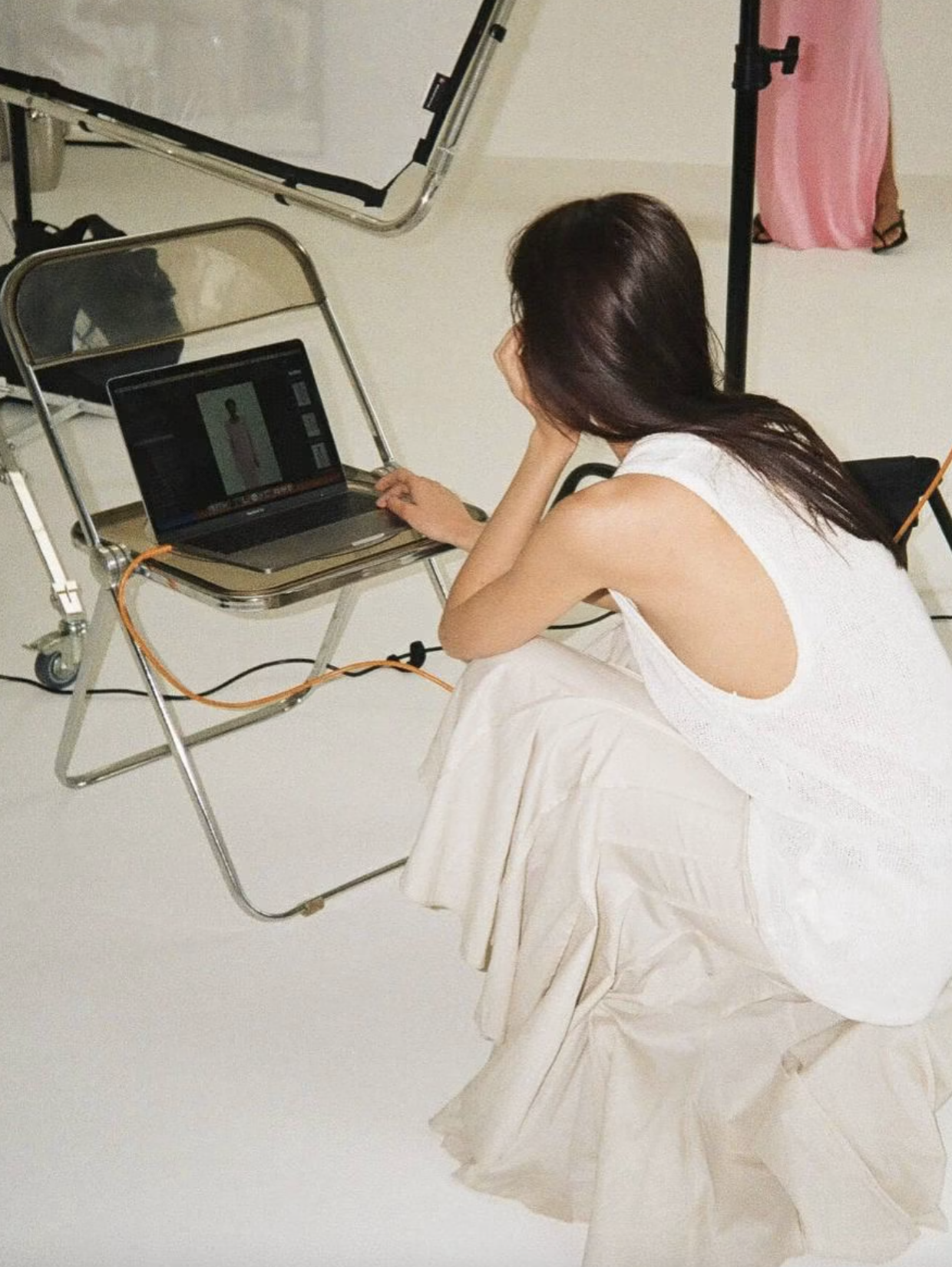 Woman sitting on the floor using a laptop during a fashion photoshoot setup in a studio showcasing AI Product Discovery.