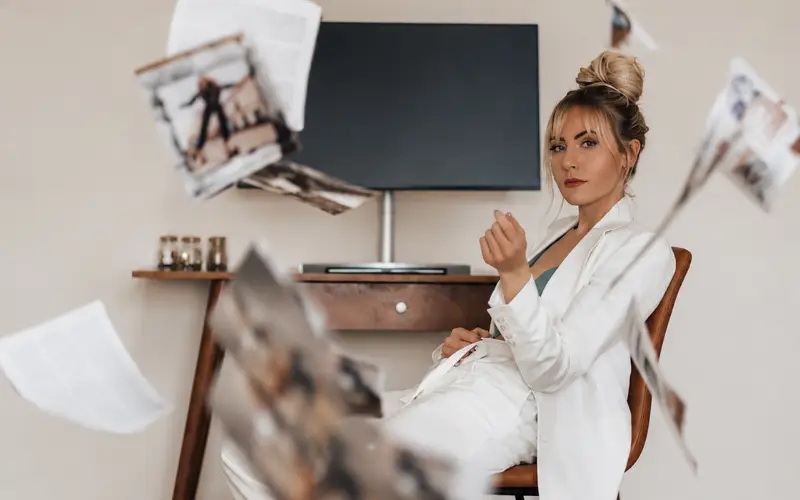 Woman in white suit surrounded by flying papers representing PR for AI Visibility and modern brand discoverability.