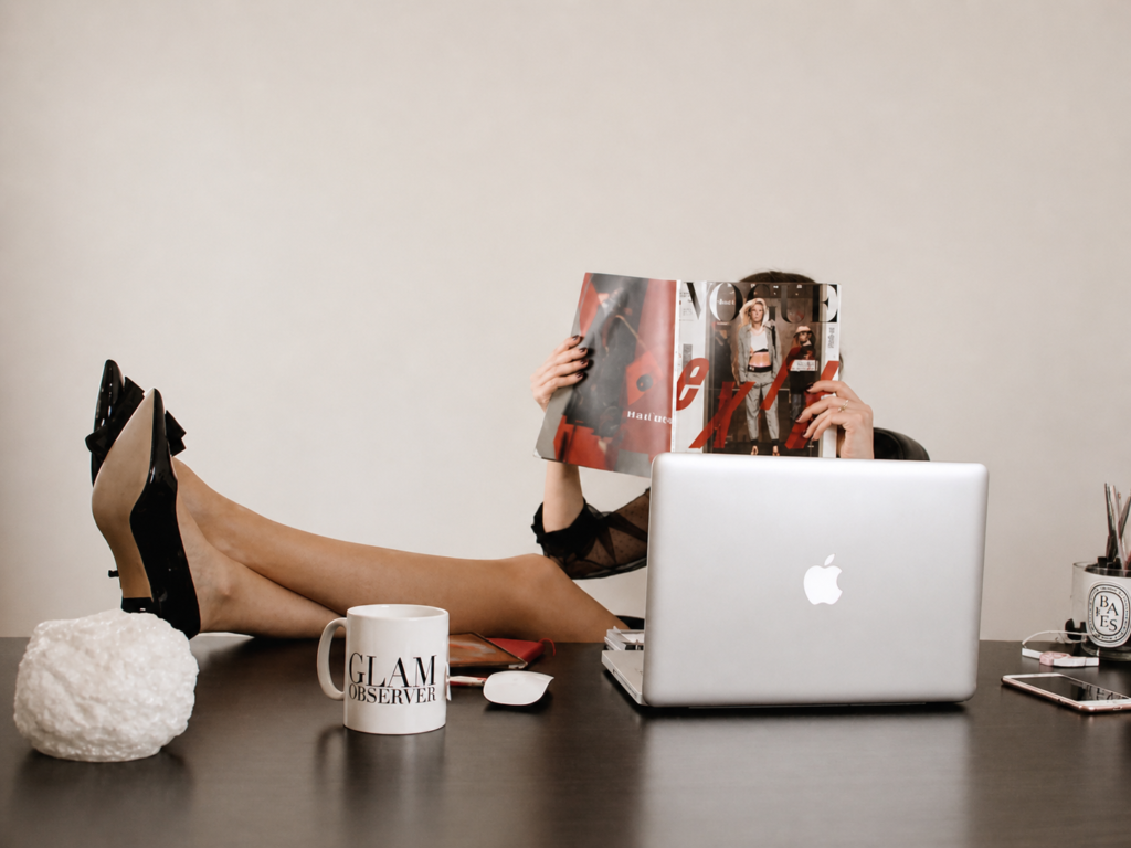 Woman reading a fashion magazine behind a laptop, representing the shift from brand visibility to digital discoverability.