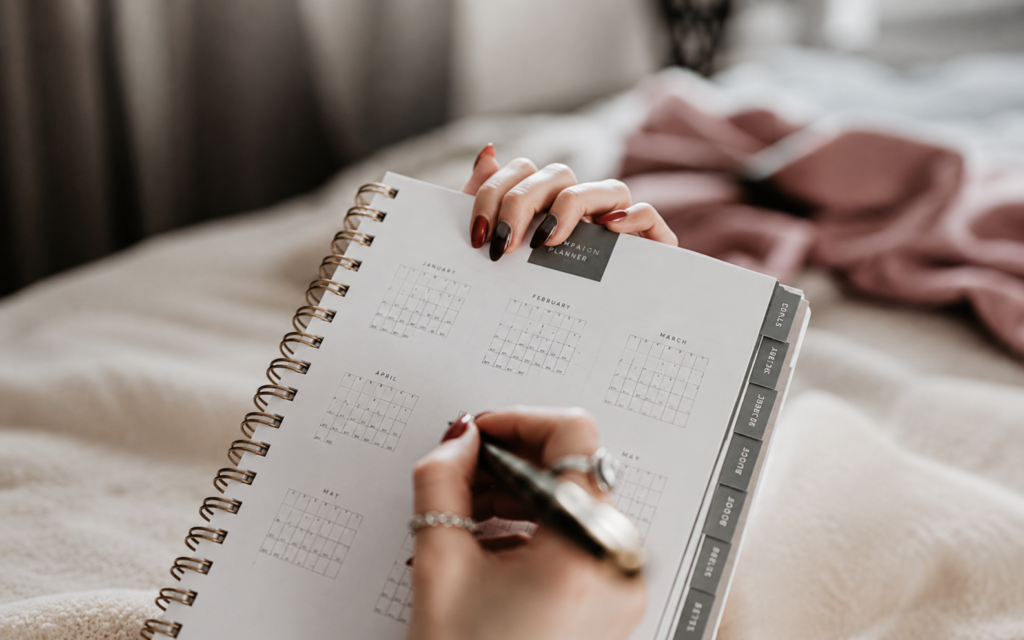 Hands writing in a campaign planner for PR goals, timelines and performance benchmarks