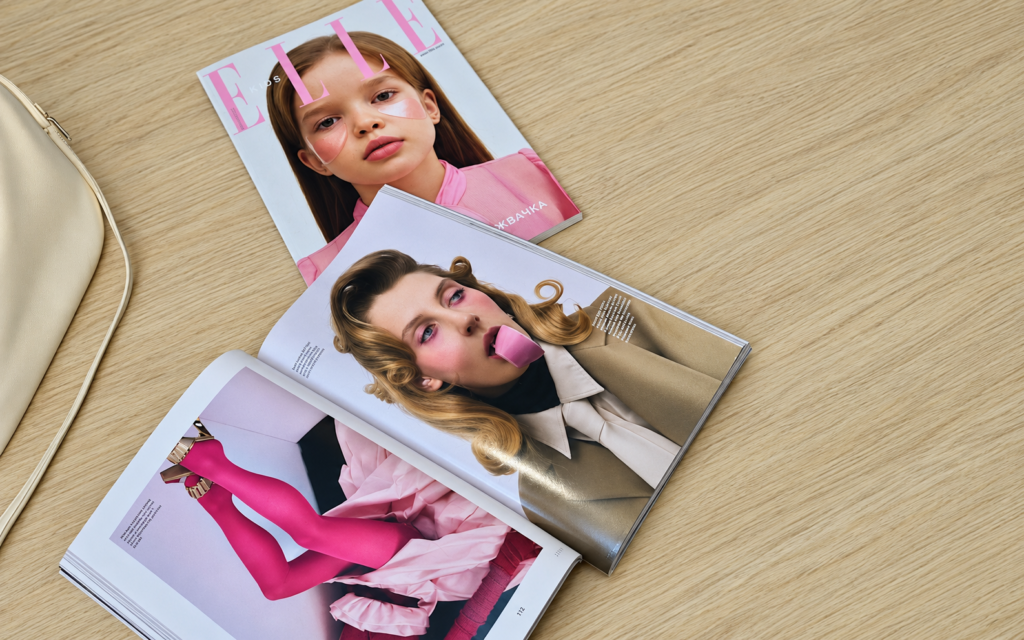 An ELLE cover and an open fashion magazine featuring pink styling on a wooden table.