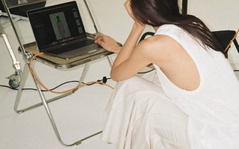 Woman sitting on the floor using a laptop during a fashion photoshoot setup in a studio showcasing AI Product Discovery.